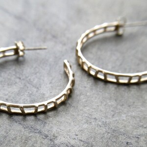 May include: A pair of gold hoop earrings with a geometric design. The earrings are made of a thin metal and have a delicate, openwork pattern.