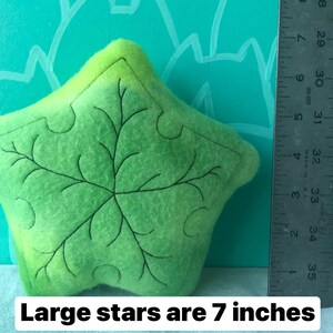 May include: A lime green star-shaped felt pillow with a black embroidered leaf design. The text "Large stars are 7 inches" is at the bottom of the image. The pillow is approximately 7 inches in size.
