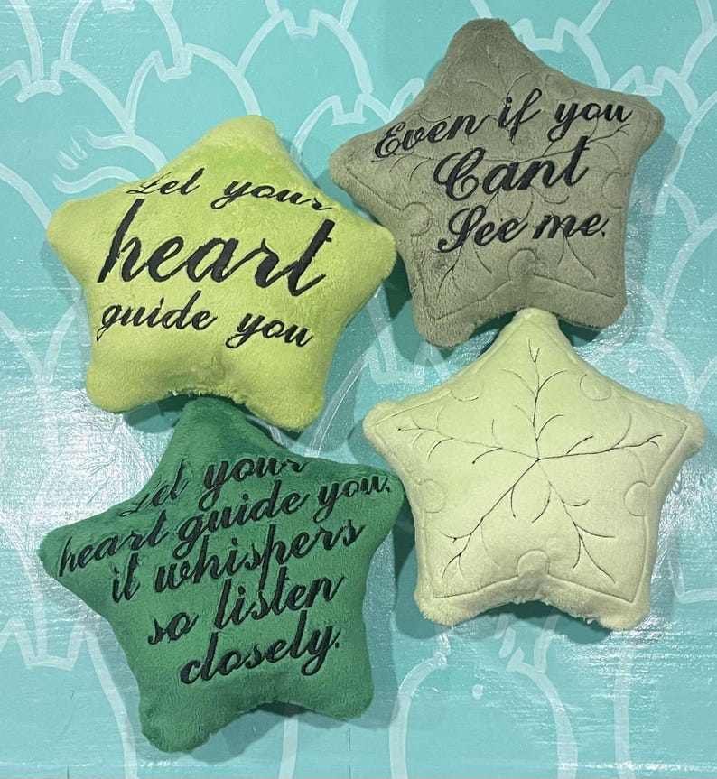 May include: Four star-shaped plush pillows in shades of green and yellow. Each pillow has embroidered text in black. One says "Let your heart guide you," another "Even if you can't see me," and a third "Let your heart guide you, it whispers so listen closely."