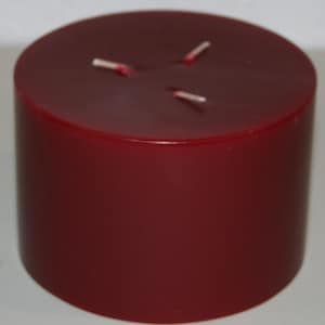 May include: A large, cylindrical, burgundy-colored candle with three wicks.