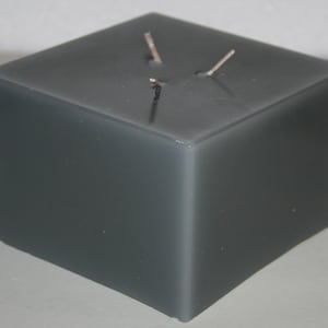 May include: A dark gray square candle with two wicks.