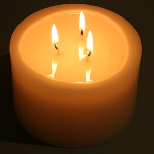 May include: A white candle with three wicks burning, casting a warm glow.