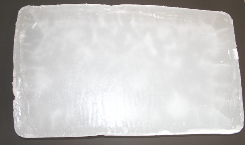 May include: A rectangular block of clear ice, with a slightly textured surface. The ice appears translucent, with subtle internal patterns. The edges are slightly uneven, suggesting it may have been cut or formed.