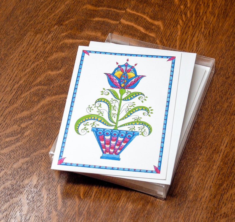 May include: A stack of blank greeting cards with a colorful illustration of a stylized flower in a pot on the front. The flower is blue, pink, yellow, and green. The pot is blue, pink, and white.