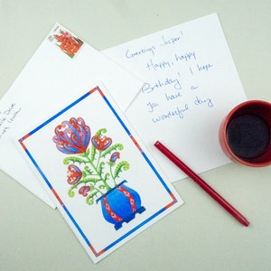 May include: A birthday card with a colorful floral illustration in a blue and red pot. The card has a handwritten message that says "Greetings Jasper! Happy, happy Birthday! I hope you have a wonderful day."