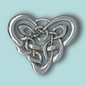 Puede incluir: Un colgante de nudo celta de plata en forma de corazón. El nudo es intrincado y detallado, con un acabado liso y pulido.