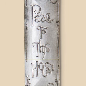 May include: A silver metal plaque with the words "Peace to this House" engraved on it. The plaque has a hole at the top for hanging.