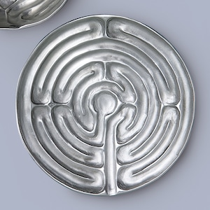 Puede incluir: Un plato circular de plata con un diseño de laberinto en relieve.