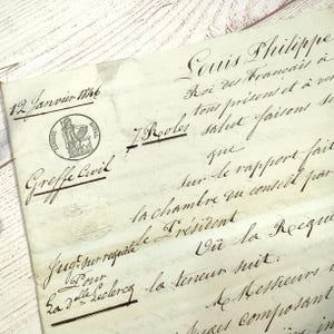 Op de afbeelding: Een antiek document met vervaagde inkt en sierlijk schrift. De tekst bevat de datum "12 Janvier 1746" en de woorden "Louis Philippe" en "Greffe Civil". Een ronde stempel met een figuur is zichtbaar.