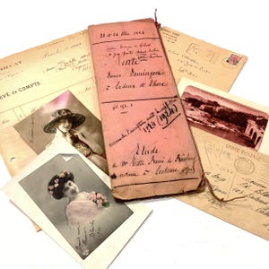 Op de afbeelding: Een verzameling vintage documenten, waaronder ansichtkaarten, brieven en een roze boekje met handgeschreven tekst. De items zijn gerangschikt op een witte ondergrond, wat een blik op het verleden biedt. De afbeelding bevat zwart-witfoto's van vrouwen.