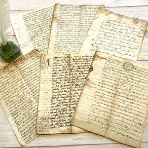 May include: A collection of aged, handwritten documents with faded ink and visible creases. The papers are arranged on a light-colored surface, with a quill and inkwell visible in the background. The script appears to be in a cursive style, suggesting historical significance.