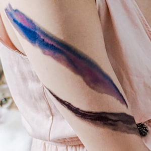 Puede incluir: Un tatuaje temporal con un diseño de acuarela de dos rayas superpuestas de azul, morado y negro.