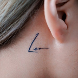 May include: A close-up of a person's ear with a small tattoo that says "Leo" behind the ear.