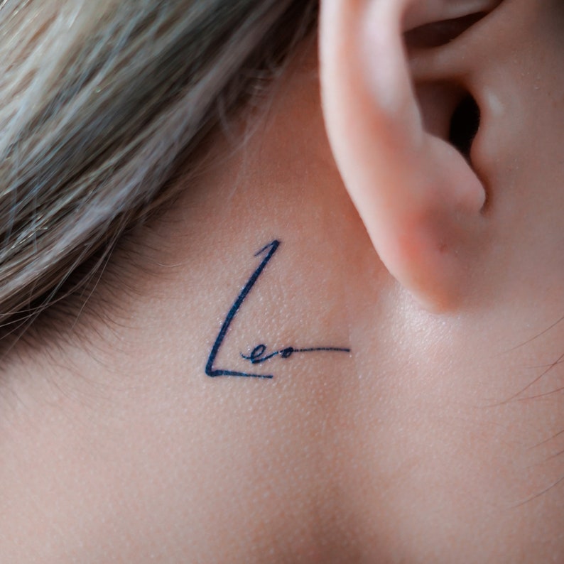May include: A close-up of a person's ear with a small tattoo that says "Leo" behind the ear.