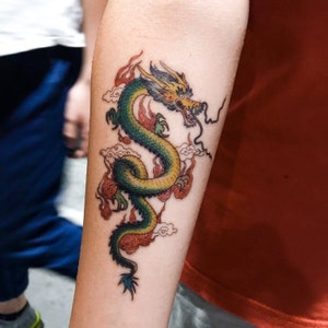 May include: A colorful tattoo of a green and yellow dragon with red flames and white clouds on a person's arm.