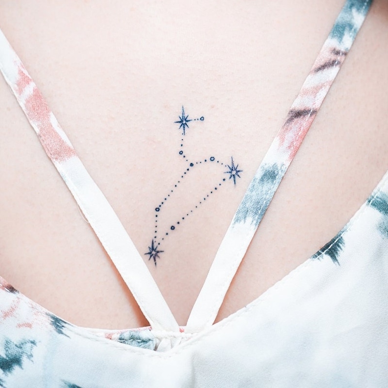 May include: A small, delicate tattoo of the constellation Leo on a person's back. The tattoo is done in black ink and features a series of small dots connected by lines to form the shape of the constellation. There are also four small stars in the tattoo.