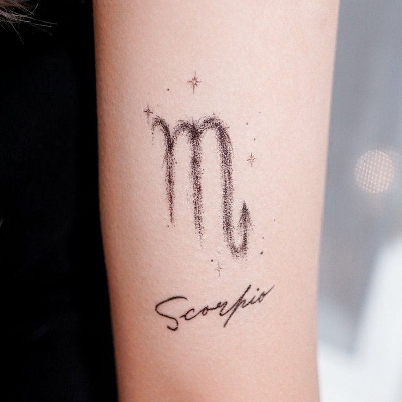 Op de afbeelding: Een zwart-witte tatoeage van het sterrenbeeld Schorpioen met het woord "Schorpioen" eronder.