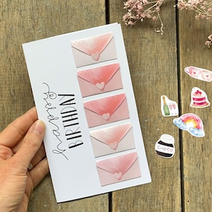 May include: A white rectangular greeting card with the text Happy Birthday in black script. The card features five pink watercolor-style envelopes arranged vertically, each adorned with a small heart detail on the flap closure.