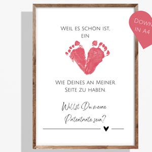 Puede incluir: Impresión enmarcada con fondo blanco y texto en alemán. La impresión presenta un corazón hecho de huellas rojas, con las palabras "Weil es schön ist, ein..." y "Willst Du meine Patentante sein?" Un corazón rosa con texto está en la parte superior derecha.