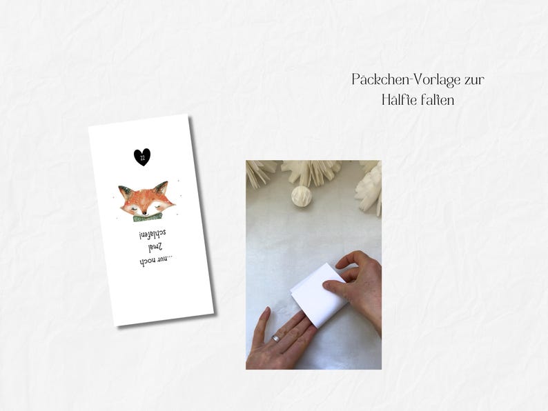 May include: A white card with a watercolor illustration of a sleeping fox with a green bow tie and the text "...nur noch schlafen!" A black heart is above the fox. The image also shows hands folding a white paper.