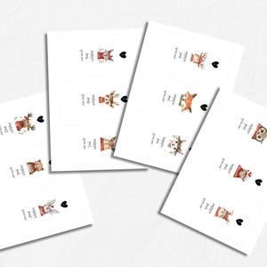 May include: White rectangular cards with watercolor illustrations of woodland animals, including a bear, fox, and owl, each wearing a winter hat. The cards have text and a black heart. The theme is likely related to winter or Christmas.