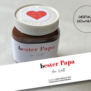Könnte beinhalten: Ein Glas Schoko-Nuss-Aufstrich mit weißem Deckel, rotem Herz und Text. Das Etikett des Glases lautet "bester Papa der Welt" in Rot und Schwarz. Eine weiße Karte zeigt denselben Text.