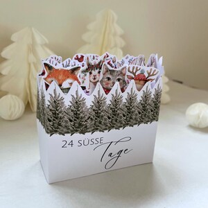 May include: White advent calendar box featuring illustrations of a fox, cat, and deer. The box is decorated with a forest scene and the text "24 Süße Tage".