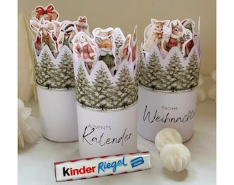 May include: Three white cylindrical Advent calendar containers with forest animal cutouts and a Kinder Riegel candy bar. The containers have a crown-shaped top with a forest scene and the words "Advents Kalender" and "Frohe Weihnachten".