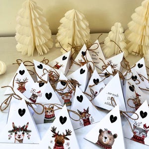 May include: Advent calendar with triangular white boxes, each adorned with a black heart and a number. The boxes feature illustrations of animals in winter attire. Paper Christmas trees and decorative balls are in the background.
