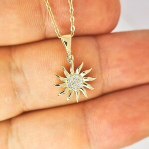 以下が含まれることがあります： 金色の太陽ペンダントネックレス。サンバーストのデザインは、複数の光線と中央の小さな透明な宝石のクラスターが特徴です。ネックレスチェーンも繊細で金色です。