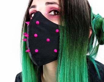 May include: A black face mask with pink spikes. The mask is worn over the lower face. The person in the image has long hair that is black at the roots and fades to bright green. The person is wearing a black button-down shirt.