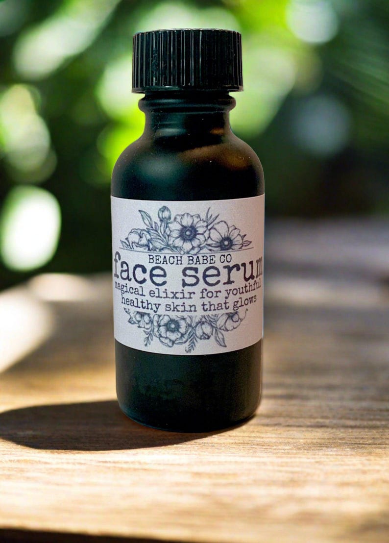 Puede incluir: Una peque&ntilde;a botella de vidrio verde oscuro con una tapa negra. La botella tiene una etiqueta blanca con texto negro que dice "Beach Babe Co. face serum magical elixir for youthful healthy skin that glows". La etiqueta est&aacute; decorada con un dise&ntilde;o floral.