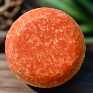May include: A round, orange-colored shampoo bar with a textured surface.
