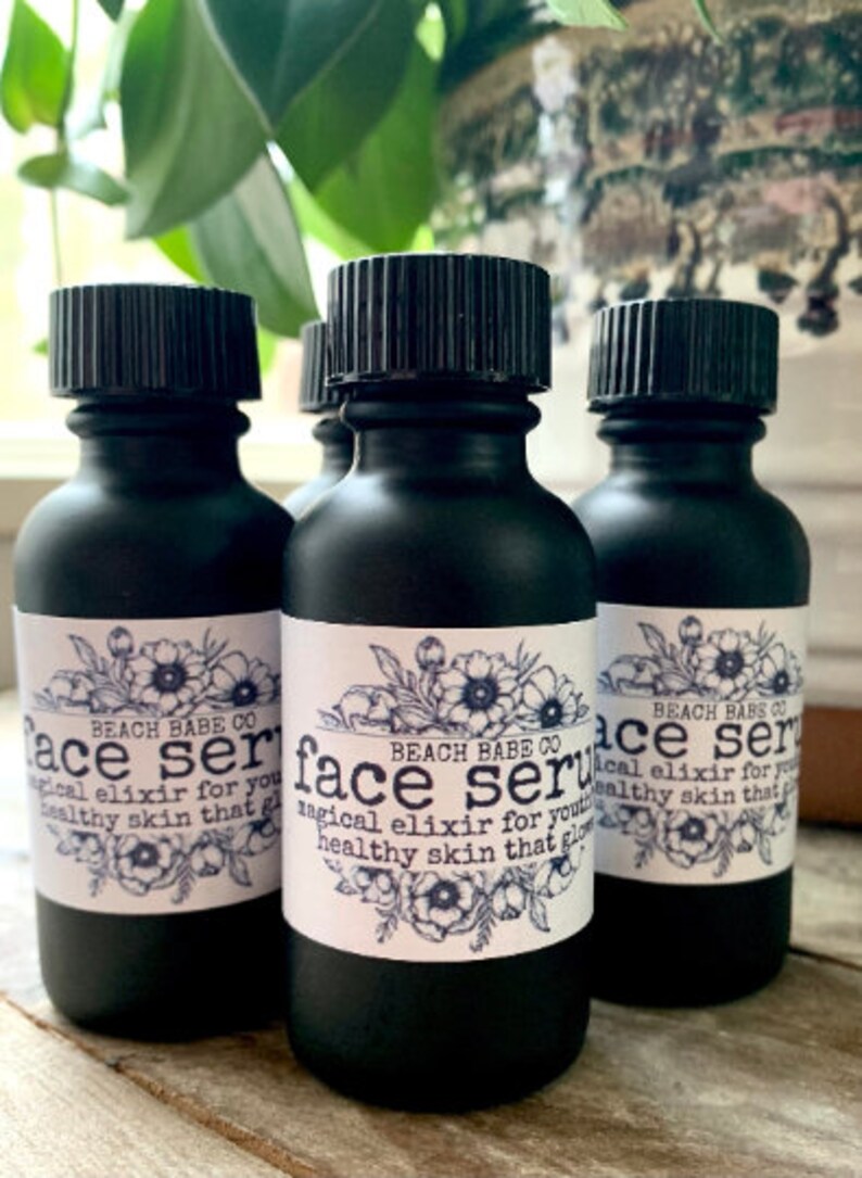 Puede incluir: Tres botellas de vidrio negro con tapas de rosca negras y etiquetas blancas. Las etiquetas tienen un dise&ntilde;o floral y el texto "BEACH BABE CO face serum magical elixir for youthful healthy skin that glows".