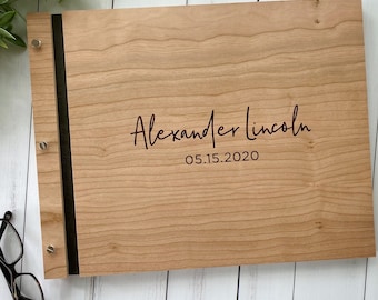 May include: A wooden photo album with a black ribbon closure. The album is personalized with the name "Alexander Lincoln" and the date "05.15.2020" in a burgundy font.