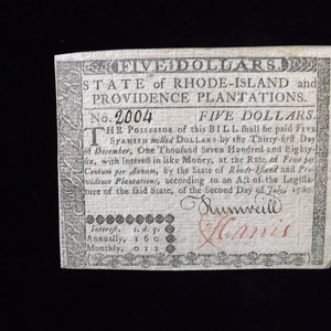 May include: A black and white historical document with the text "FIVE DOLLARS. STATE of RHODE-ISLAND and PROVIDENCE PLANTATIONS. No. 2004 FIVE DOLLARS. THE POSSESSOR of this BILL shall be paid FIVE SPANISH milled DOLLARS by the Thirty-first Day of December, One Thousand Seven Hundred and Eighty-six, with Interest in like Money, at the Rate of Five per Centum per Annam, by the State of Rhode Island and Providence Plantations, according to an Act of the Legislature of the said State, of the Second Day of July, 1780. Interest. s. d. q. Annually, 1 6 0 Monthly, 0 1 2" and two signatures, "Sumveill" and "Hanis".