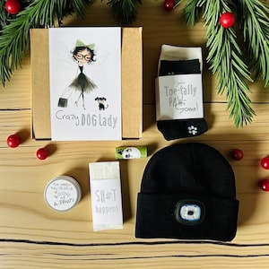Peut inclure: Un coffret cadeau pour les amoureux des chiens, comprenant une boîte avec une illustration "Crazy Dog Lady", des chaussettes avec des empreintes de pattes, un bonnet noir avec une lumière, un baume à lèvres et un petit récipient.