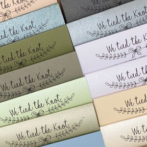 Puede incluir: Una pila de tarjetas con diferentes fondos de colores. Cada tarjeta tiene el texto "We tied the knot" con un dise&ntilde;o floral decorativo.