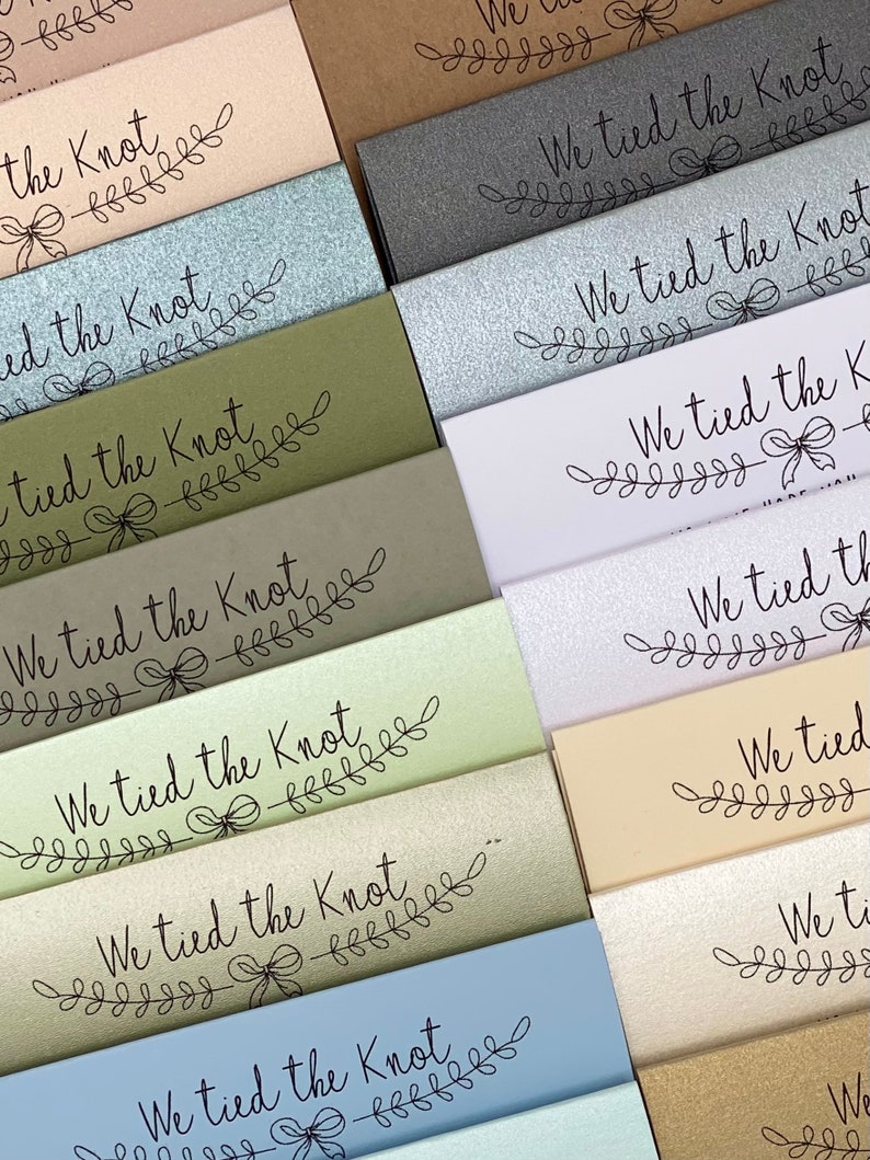 Puede incluir: Una pila de tarjetas con diferentes fondos de colores. Cada tarjeta tiene el texto "We tied the knot" con un dise&ntilde;o floral decorativo.