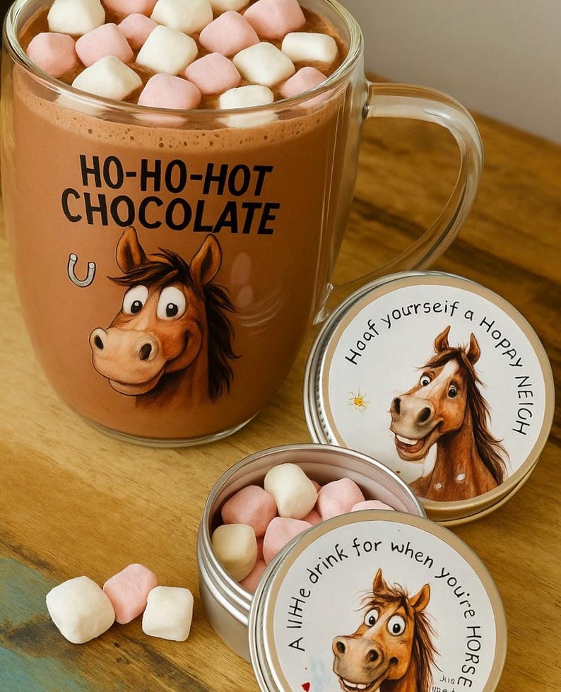 May include: A clear glass mug filled with hot chocolate and topped with pink and white marshmallows. The mug has a horse graphic and the text "HO-HO-HOT CHOCOLATE." Two small tins with horse graphics and text are also present.