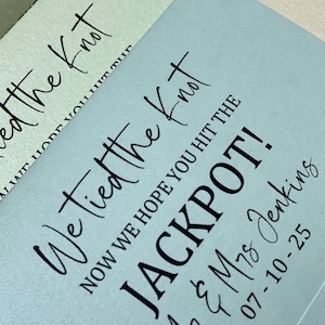 Puede incluir: Una tarjeta azul claro con el texto "We tied the knot, now we hope you hit the jackpot!" La tarjeta tambi&eacute;n incluye los nombres "M7 & M78 Jenkins" y la fecha "07-10-25".