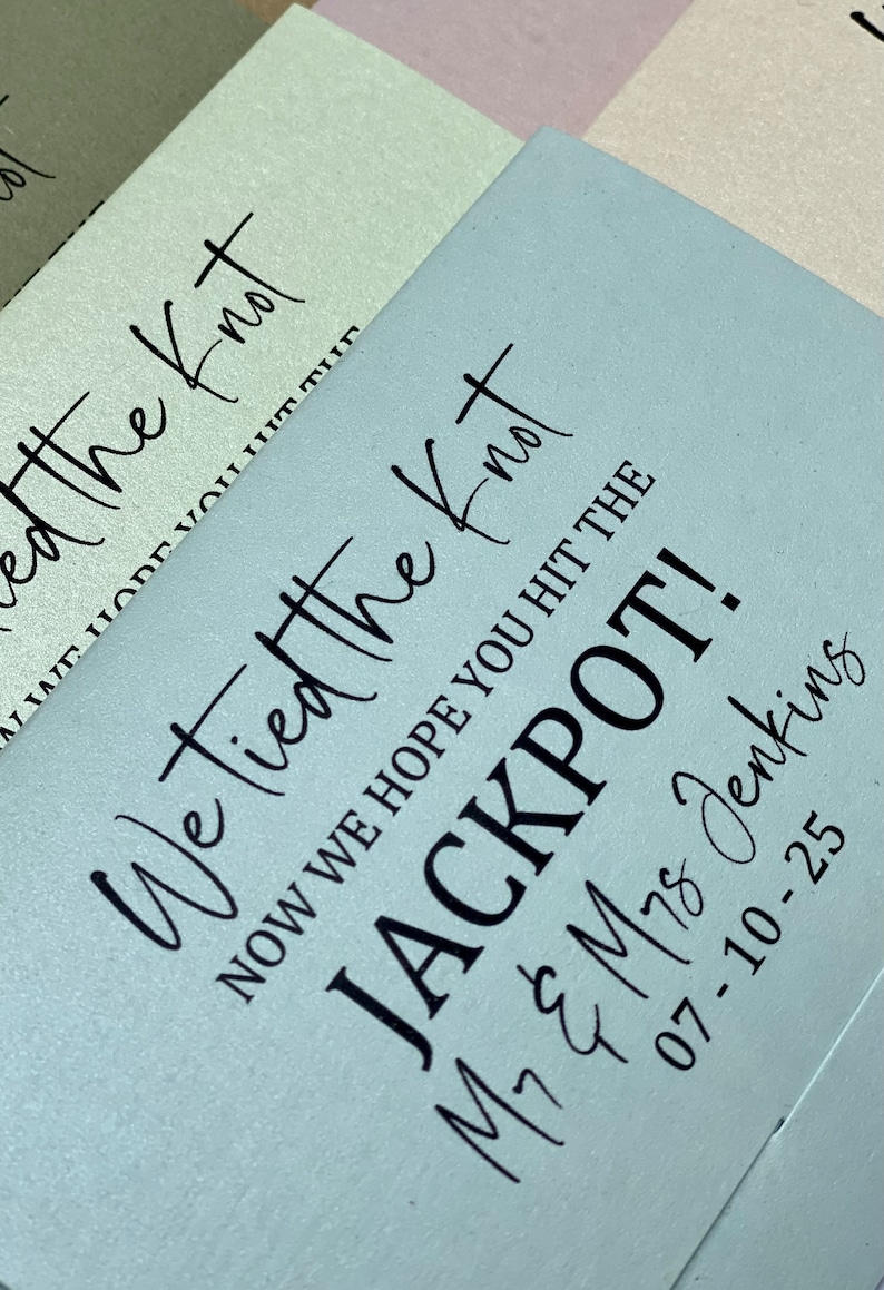 Puede incluir: Una tarjeta azul claro con el texto "We tied the knot, now we hope you hit the jackpot!" La tarjeta tambi&eacute;n incluye los nombres "M7 & M78 Jenkins" y la fecha "07-10-25".