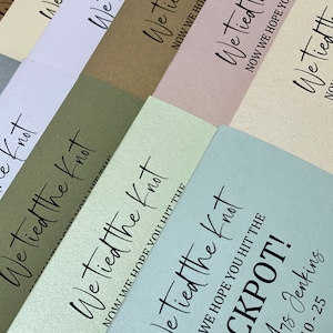 Puede incluir: Una pila de sobres de color azul claro, blanco, verde, marr&oacute;n, rosa y crema con el texto "We tied the knot" y "Now we hope you hit the jackpot!" impreso en ellos.