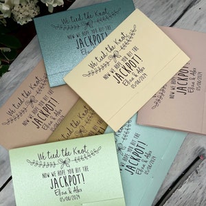 Puede incluir: Un conjunto de seis sobres de regalo de boda con fondo azul claro, verde, beige y rosa. Los sobres tienen un dise&ntilde;o en blanco y negro con el texto "We tied the knot" y "Now we hope you hit the jackpot!" con los nombres de la pareja y la fecha de la boda.