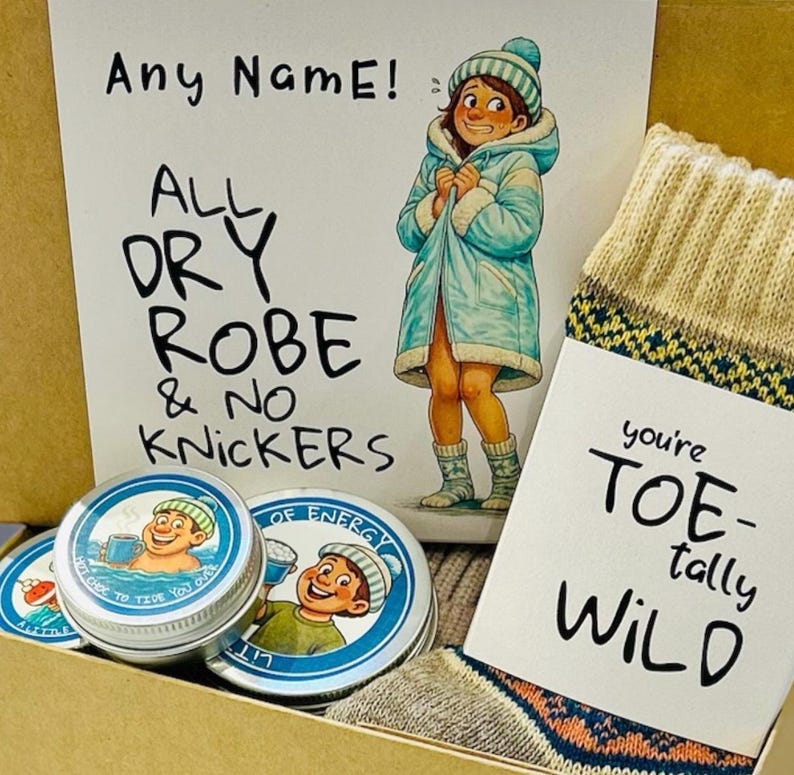 Pu&ograve; includere: Una confezione regalo con un'illustrazione a cartoni animati di una persona in accappatoio e il testo "Any Name! All Dry Robe & No Knickers". Include due piccole lattine e un paio di calzini con la scritta "you're Toe-tally Wild".