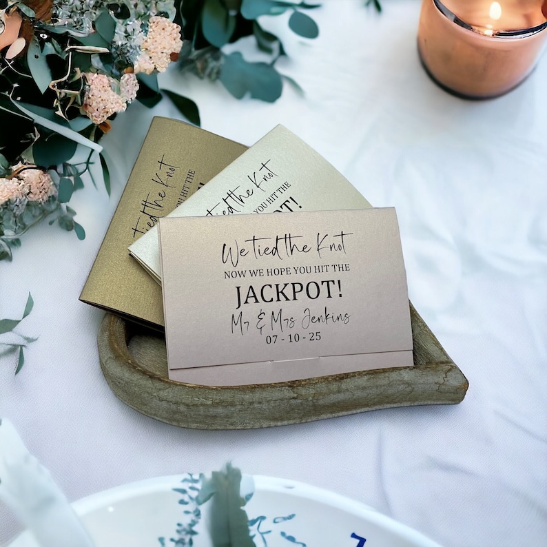 Puede incluir: Una tarjeta rosa con el texto "We tied the knot now we hope you hit the jackpot! Mr. & Mrs. Jenkins 07-10-25" en letras negras. La tarjeta est&aacute; sobre una bandeja de madera en forma de coraz&oacute;n.