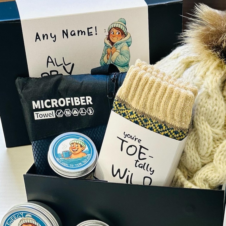 Pu&ograve; includere: Una confezione regalo nera contiene un asciugamano in microfibra, un paio di calzini beige con un motivo e una lattina di cioccolata calda. &Egrave; inclusa anche una carta con il testo "Any Name!" e un'illustrazione invernale.