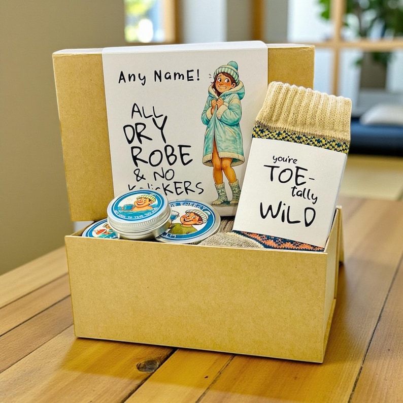Pu&ograve; includere: Una confezione regalo con un'illustrazione a cartoni animati di una persona in accappatoio. La scatola contiene calzini con la scritta "you're toe-tally WILD", burrocacao e adesivi rotondi. La scatola riporta la scritta "Any Name! ALL DRY ROBE & NO -ckers".