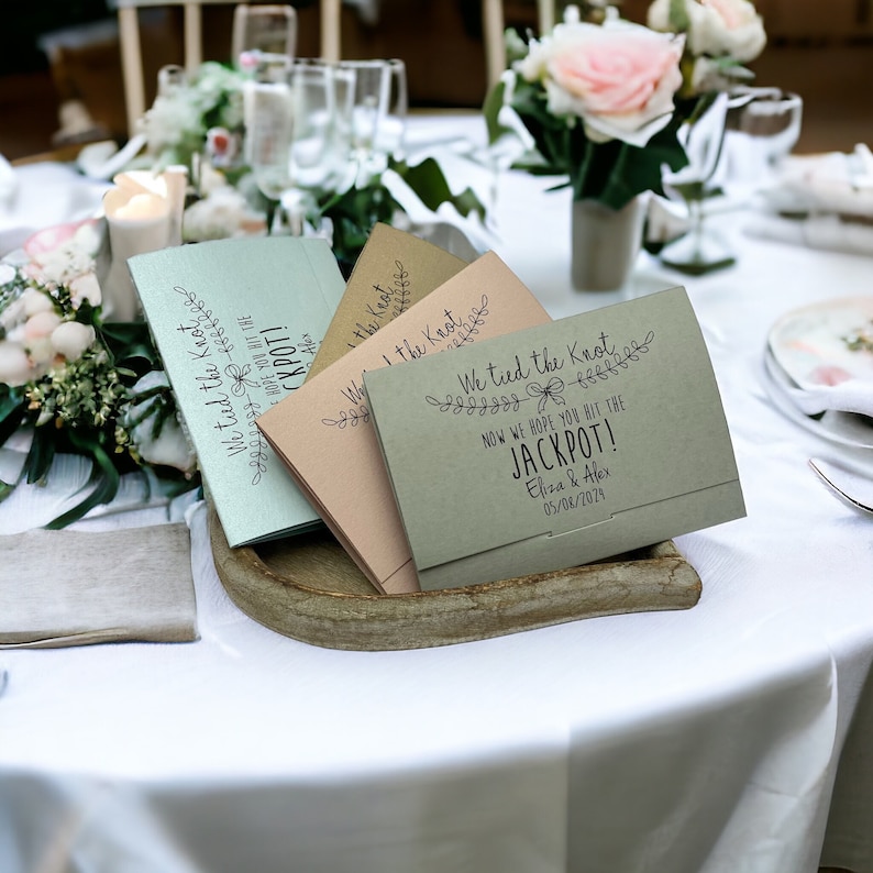 Puede incluir: Sobres de regalo de boda verdes, marrones y azules con el texto "We tied the knot" y "Now we hope you hit the jackpot!" con la fecha 05/08/2074.