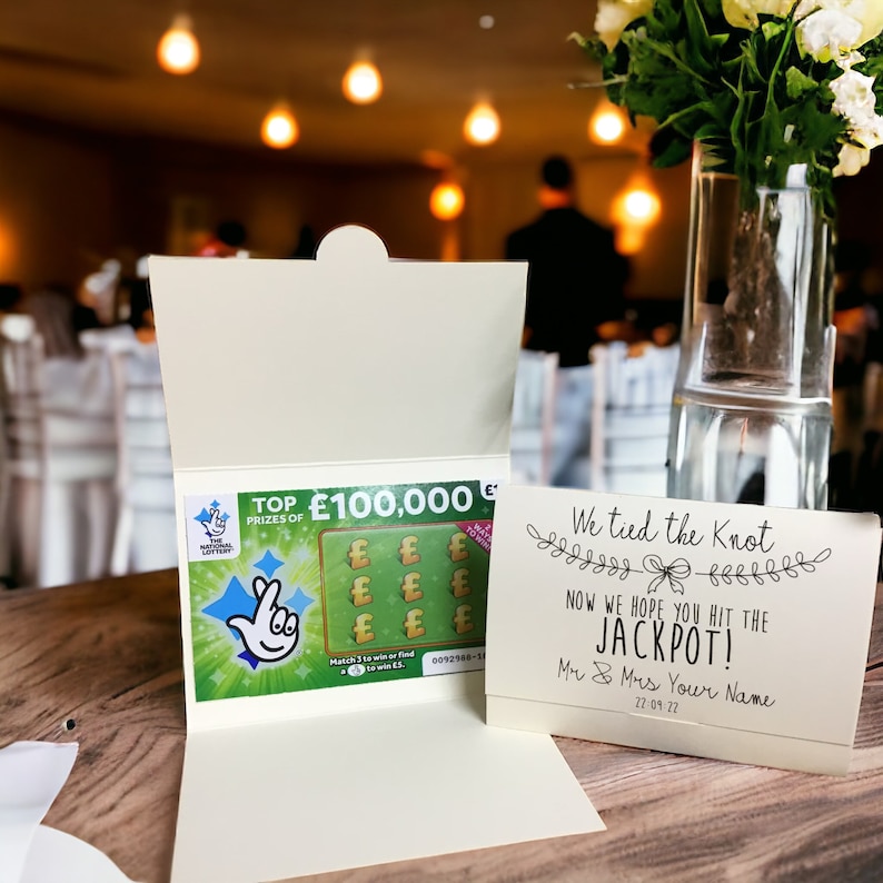 Puede incluir: Una tarjeta blanca con un billete de loter&iacute;a verde en su interior. El billete de loter&iacute;a tiene una imagen de una mano con un dedo apuntando a una estrella. El texto en la tarjeta dice "We tied the knot" y "Now we hope you hit the jackpot!" con la fecha "22 09 27".